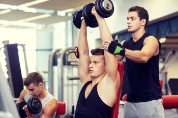 sport, fitness, lifestyle, powerlifting and people concept - group of men with dumbbells and personal trainer flexing muscles in gym