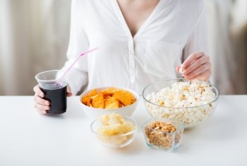 people, fast food, junk-food and unhealthy eating concept - close up of woman with popcorn, nachos or corn crisps and peanuts in bowls