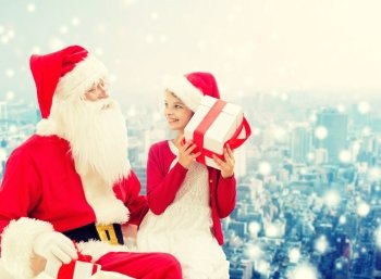 holidays, christmas, childhood and people concept - smiling little girl with santa claus and gifts over snowy city background