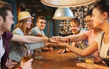 people, leisure, friendship and gesture concept - group of happy smiling friends with drinks putting hands on top of each other at bar or pub