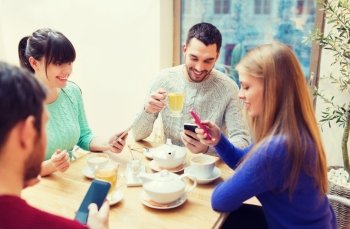 people, leisure, friendship and technology concept - group of happy friends with smartphones meeting at cafe and drinking tea