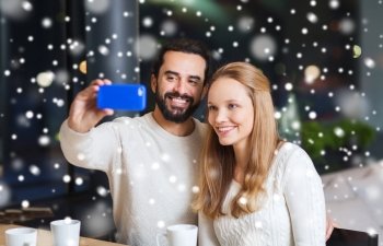 people, leisure, communication, technology and season - happy couple with smartphone taking selfie at winter cafe