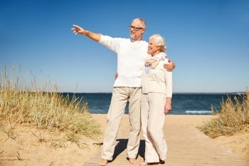family, age, travel, tourism and people concept - happy senior couple pointing finger to something on summer beach