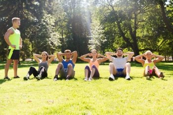 fitness, sport, friendship and healthy lifestyle concept - group of happy teenage friends or sportsmen exercising and doing sit-ups at boot camp