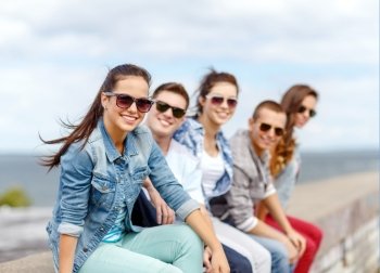 summer holidays and teenage concept - smiling teenage girl in sunglasses hanging out with friends outdoors. smiling teenage girl hanging out with friends