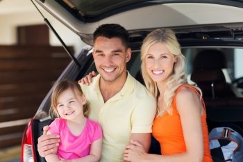 transport, leisure, road trip and people concept - happy family with little girl sittin on open hatchback car  trunk at home parking space