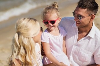 family, vacation, adoption and people concept - happy man, woman and little girl in sunglasses talking on summer beach