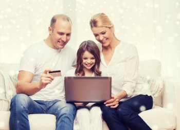 family, shopping, technology and people concept - happy family with laptop computer and credit card over snowflakes background