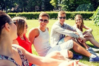 friendship, leisure, summer and people concept - group of smiling friends outdoors sitting and talking on grass on grass in park