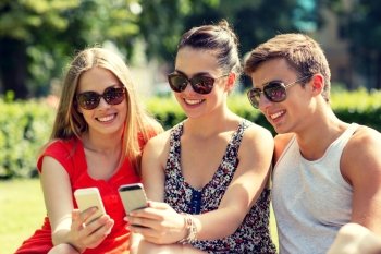 friendship, leisure, summer, technology and people concept - group of smiling friends with smartphone sitting on grass in park