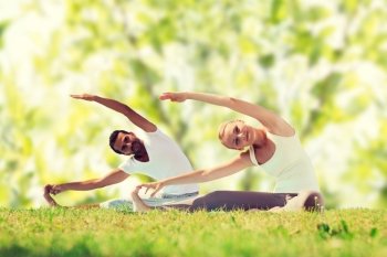 fitness, sport, yoga and people concept - happy couple stretching on mats over green tree leaves background