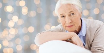 age and people concept - happy smiling senior woman face over holidays lights background. happy senior woman resting on sofa over lights
