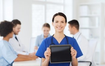 clinic, profession, people and medicine concept - happy female doctor showing tablet pc computer blank screen over group of medics meeting at hospital