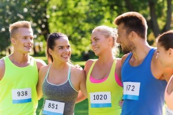 fitness, sport, marathon, friendship and healthy lifestyle concept - group of happy teenage friends or sportsmen couple with racing badge numbers outdoors