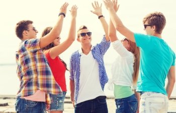 friendship, leisure, summer, gesture and people concept - group of smiling friends making high five outdoors