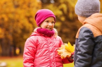 childhood, leisure, friendship and people concept - happy little boy giving maple leaves to girl in autumn park