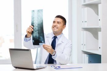 healthcare, technology, rontgen, people and medicine concept - smiling male doctor in white coat with laptop computer looking at x-ray in medical office