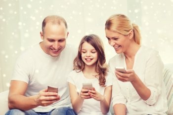 family, home, technology and people concept - smiling mother, father and little girl with smartphones over snowflakes background
