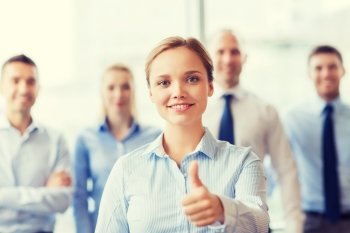 business, people, gesture and teamwork concept - smiling businesswoman showing thumbs up with group of businesspeople in office