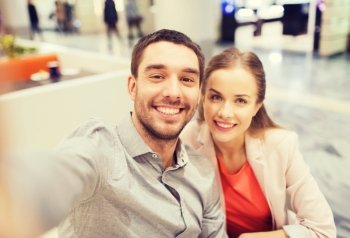 technology, photographing, and people concept - happy couple taking selfie with smartphone or camera in mall