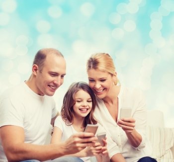family, holidays, technology and people concept - smiling mother, father and little girl with smartphones over blue lights background