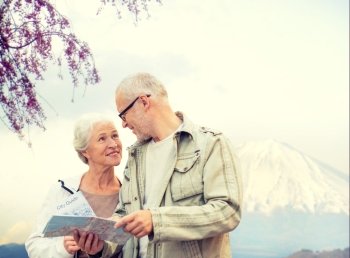 family, age, tourism, travel and people concept - senior couple with map and city guide talking over japan mountains background