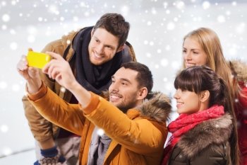 people, friendship, technology and leisure concept - happy friends taking selfie with smartphone on skating rink