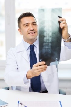 healthcare, rontgen, people and medicine concept - smiling male doctor in white coat looking at x-ray in medical office