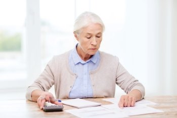 business, savings, annuity insurance, age and people concept - senior woman with papers or bills and calculator writing at home