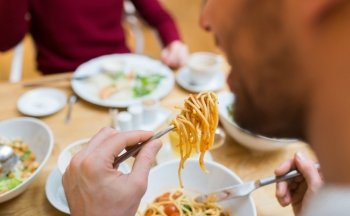 people, leisure and food concept - close up man eating pasta for dinner at restaurant or home