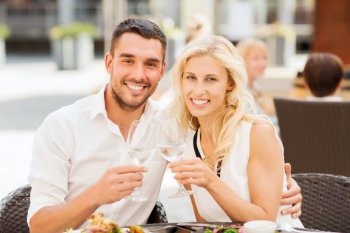 love, dating, people and holidays concept - smiling couple clinking glasses and looking to each other at restaurant lounge or terrace