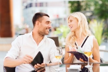 date, people, payment and financial independence concept - happy couple with cash money in wallets and wine glasses paying bill at restaurant