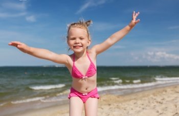 summer, childhood, vacation and people concept - happy little girl in swimwear having fun on beach