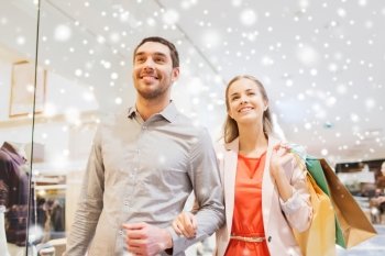 sale, consumerism and people concept - happy young couple with shopping bags walking in mall with snow effect
