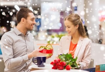 love, romance, valentines day, couple and people concept - happy young couple with red flowers and open gift box in at cafe mall with snow effect