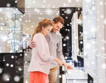 sale, consumerism, shopping and people concept - happy couple choosing engagement ring at jewelry store in mall with snow effect