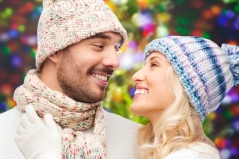 winter, fashion, couple, christmas and people concept - smiling man and woman in hats and scarf over holidays lights background