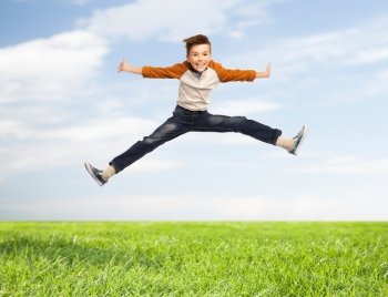 happiness, childhood, freedom, movement and people concept - happy smiling boy jumping in air over blue sky and grass background