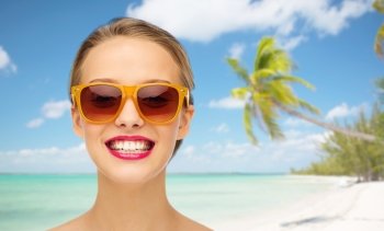 people, accessory, summer vacation, travel and fashion concept - smiling young woman in sunglasses with pink lipstick on lips over tropical beach with palm background