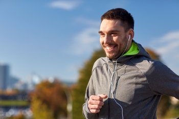 fitness, sport, people, technology and lifestyle concept - happy man running and listening to music in earphones at city