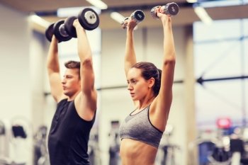 sport, fitness, lifestyle and people concept - smiling man and woman with dumbbells flexing muscles in gym