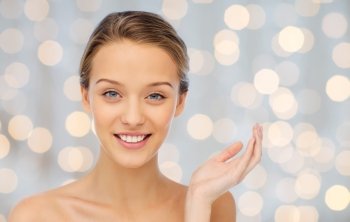 beauty, people and health concept - smiling young woman face and shoulders over holidays lights background