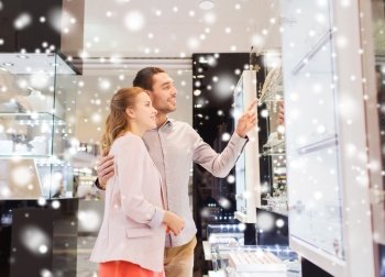 sale, consumerism and people concept - happy couple pointing finger to shopping window at jewelry store in mall with snow effect
