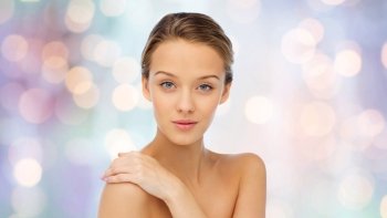 beauty, people, body care and health concept - smiling young woman face and hand on bare shoulder over purple holidays lights background