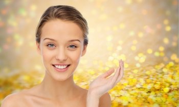 beauty, people and health concept - smiling young woman face and shoulders over golden glitter or holidays lights background