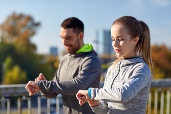 fitness, sport, people, technology and healthy lifestyle concept - smiling couple with heart-rate watch running over city highway bridge