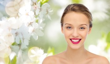 beauty, people and health concept - smiling young woman face with pink lipstick on lips and shoulders over summer green natural background with cherry blossom