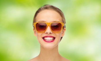 beauty, people, accessory and fashion concept - smiling young woman in sunglasses with pink lipstick on lips over green summer background