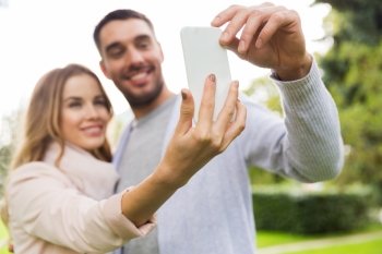 love, relationship, technology and people concept - close up of happy couple with smartphone taking selfie in summer park