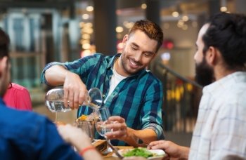 leisure, people and holidays concept - smiling man with friends pouring water from jug at restaurant